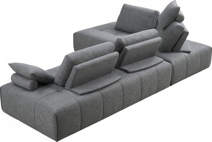 Sofá modular en forma de L de dos piezas de poliéster gris con chaise longue y cojines.